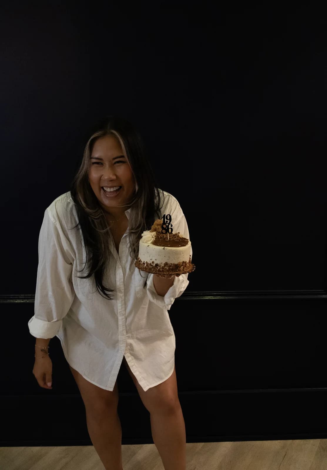 Candid shot of a woman laughing and leaning toward the camera with a birthday cake held at her side.
