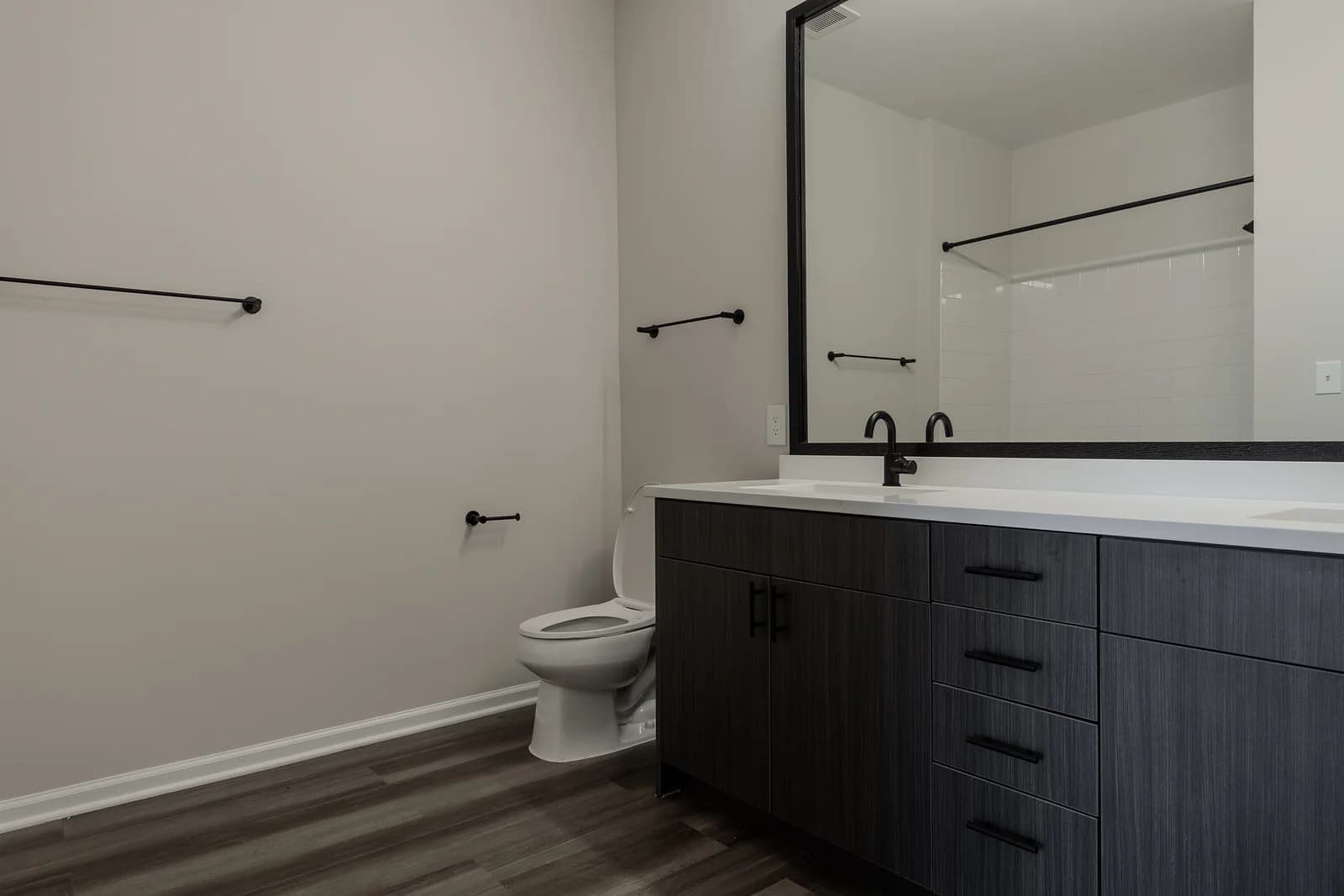Bathroom with a dark double vanity, black-framed mirror, matte black faucets and towel bars, and a white toilet.