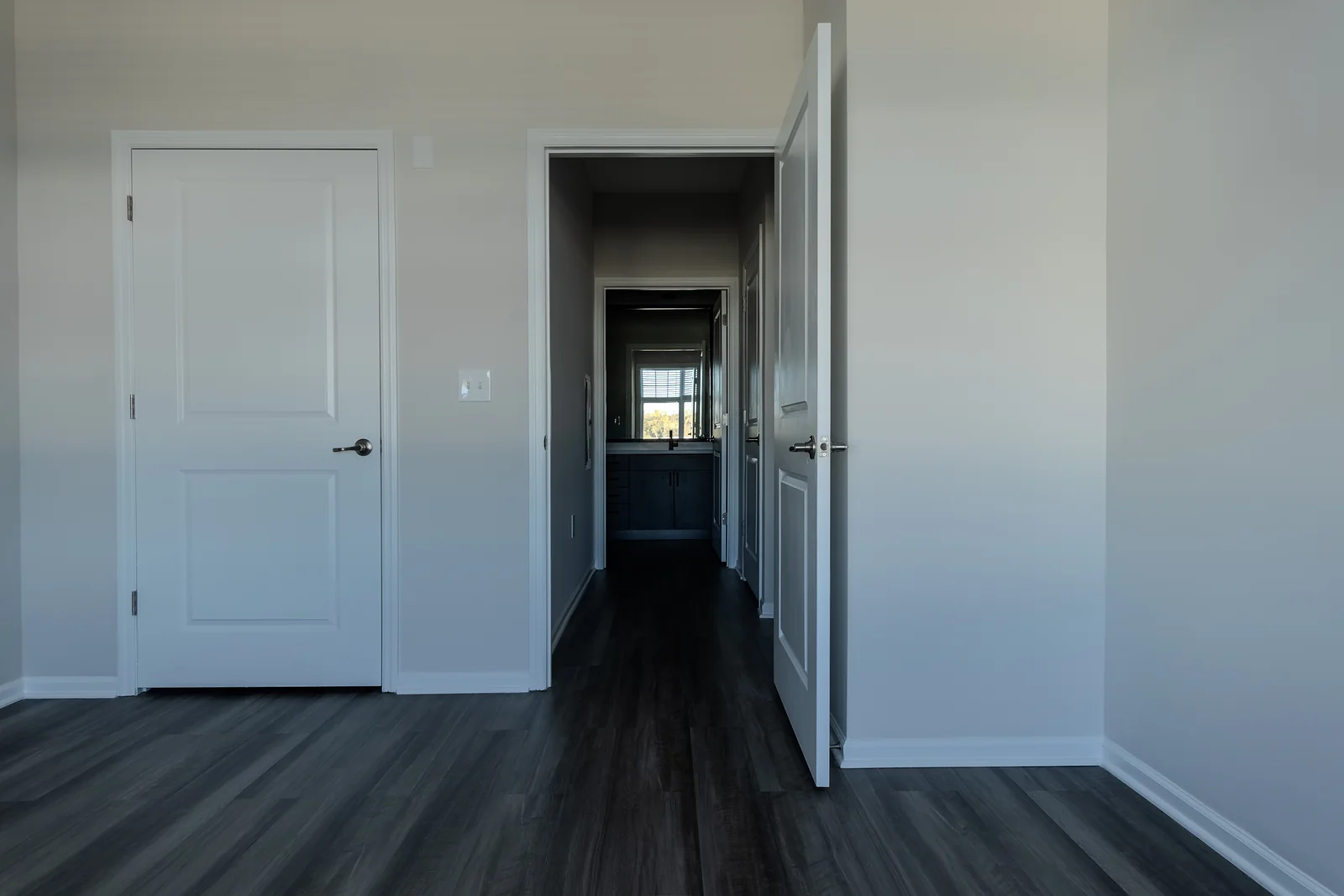 Bedroom corner with white paneled doors and an open doorway looking down a hallway toward a window.