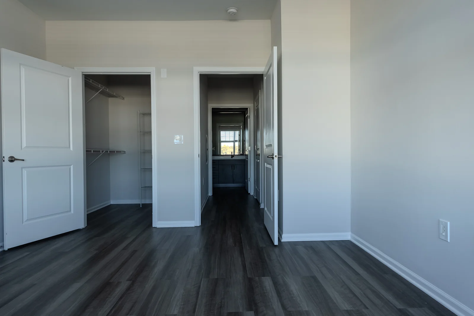 Bedroom with an open walk-in closet with wire shelving beside a doorway leading down a hallway.