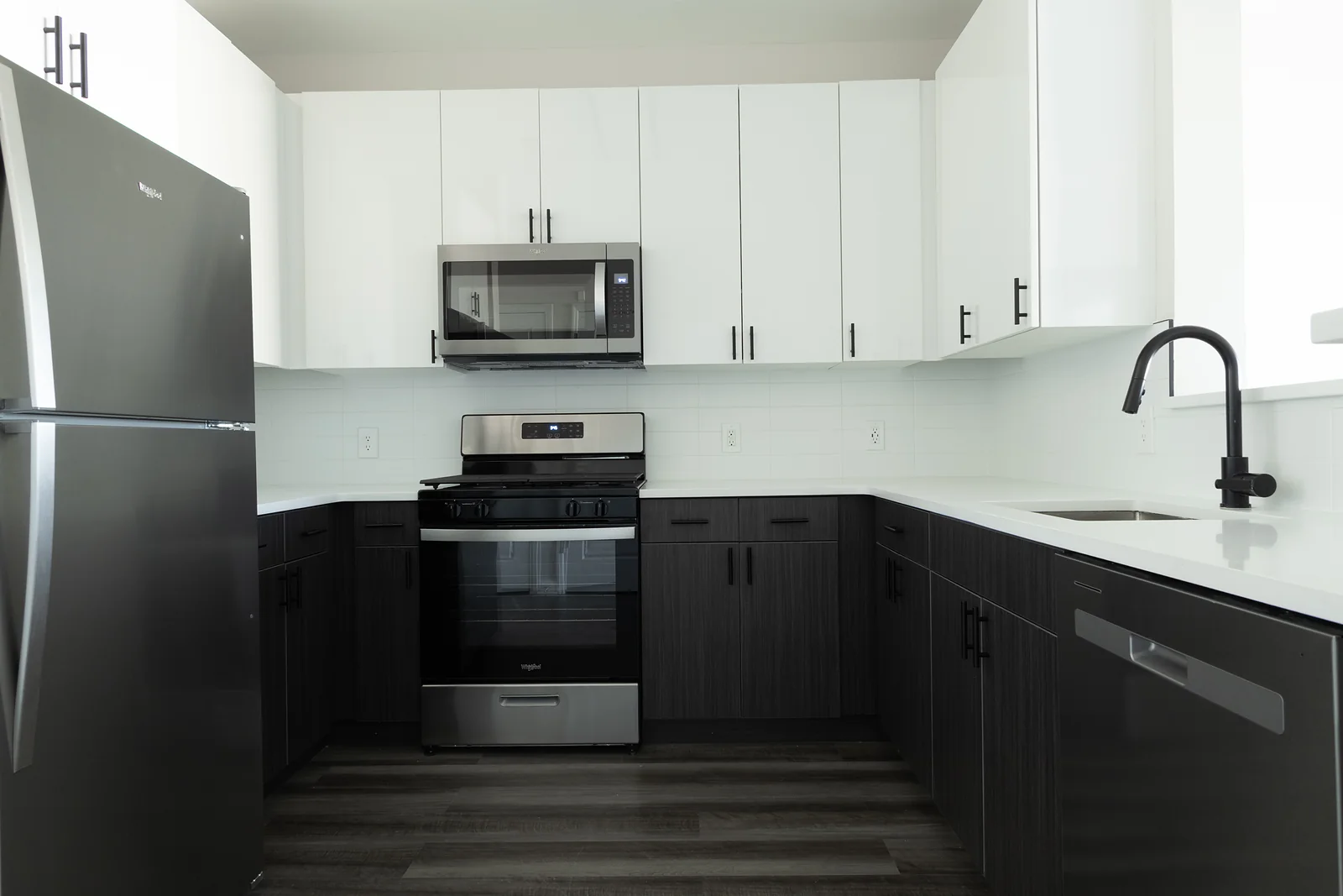 L-shaped kitchen with white upper cabinets, dark lower cabinets, white countertops, and a stainless steel gas range and microwave.