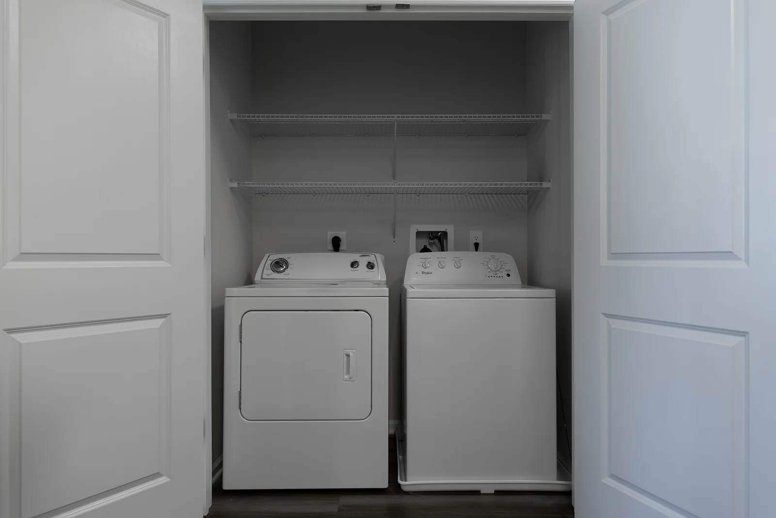 Laundry closet with white double doors open to a washer, dryer, and wire shelving above.