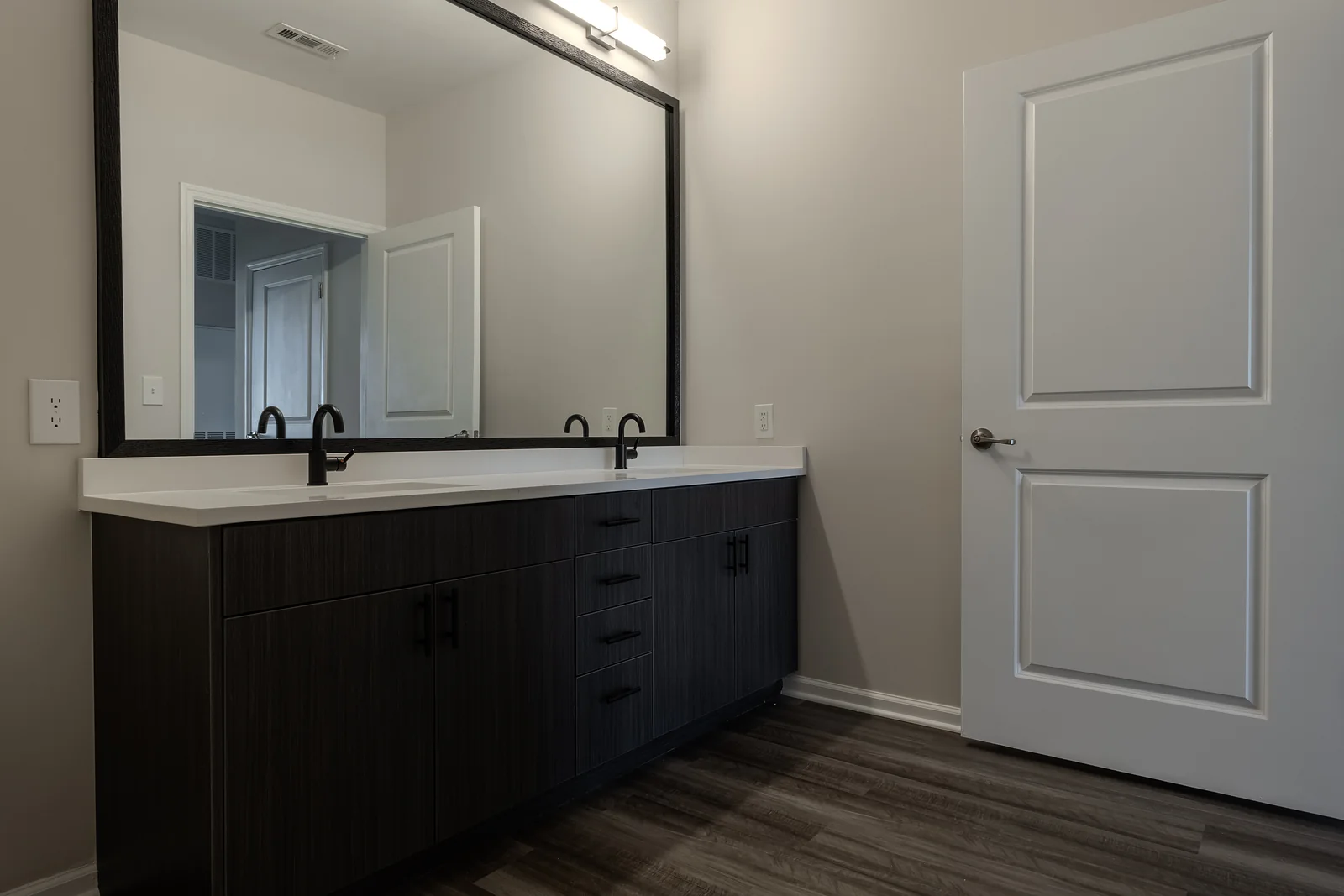 Bathroom with a dark wood double vanity, white countertop, matte black faucets, and a large black-framed mirror.
