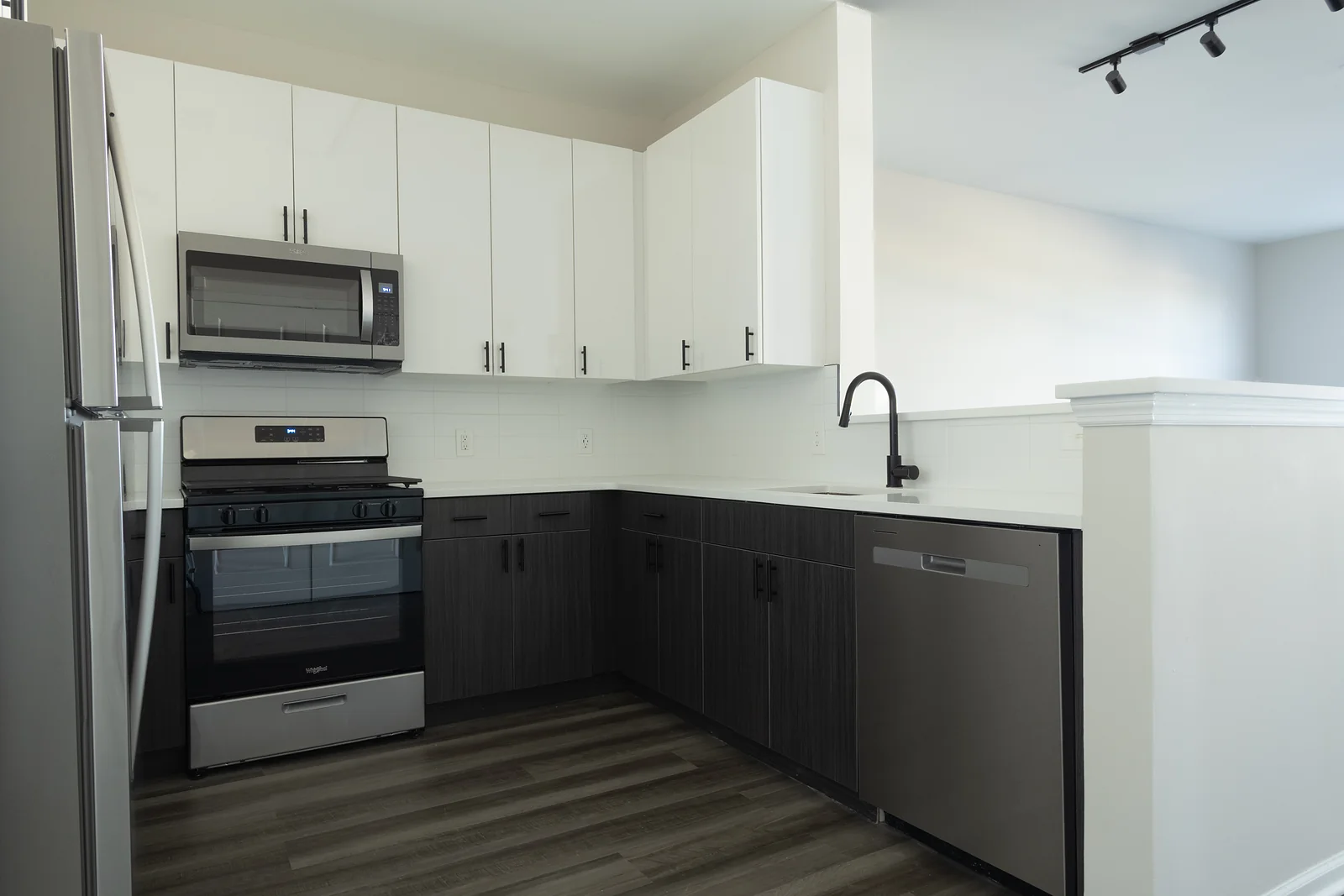 Modern kitchen with white upper cabinets, dark lower cabinets, and stainless steel range, microwave, dishwasher, and refrigerator.