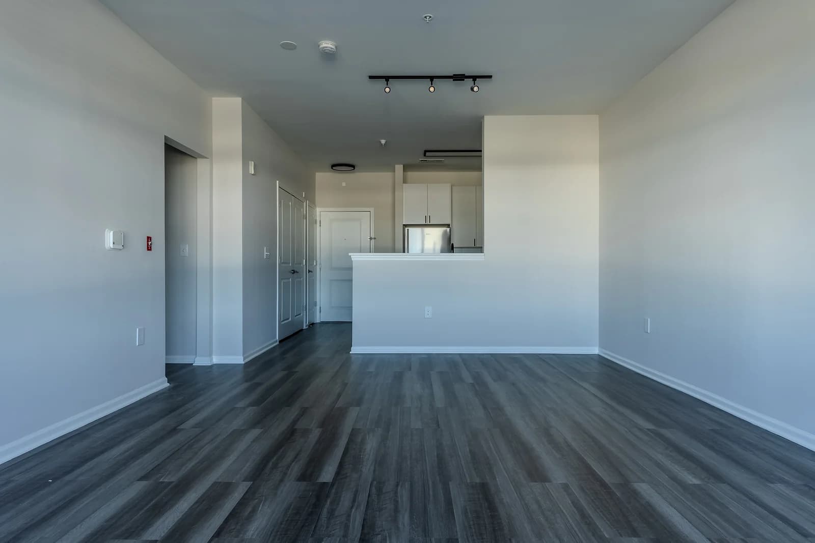 Open-concept living room looking toward the kitchen, with a breakfast bar, track lighting, and gray plank floors.