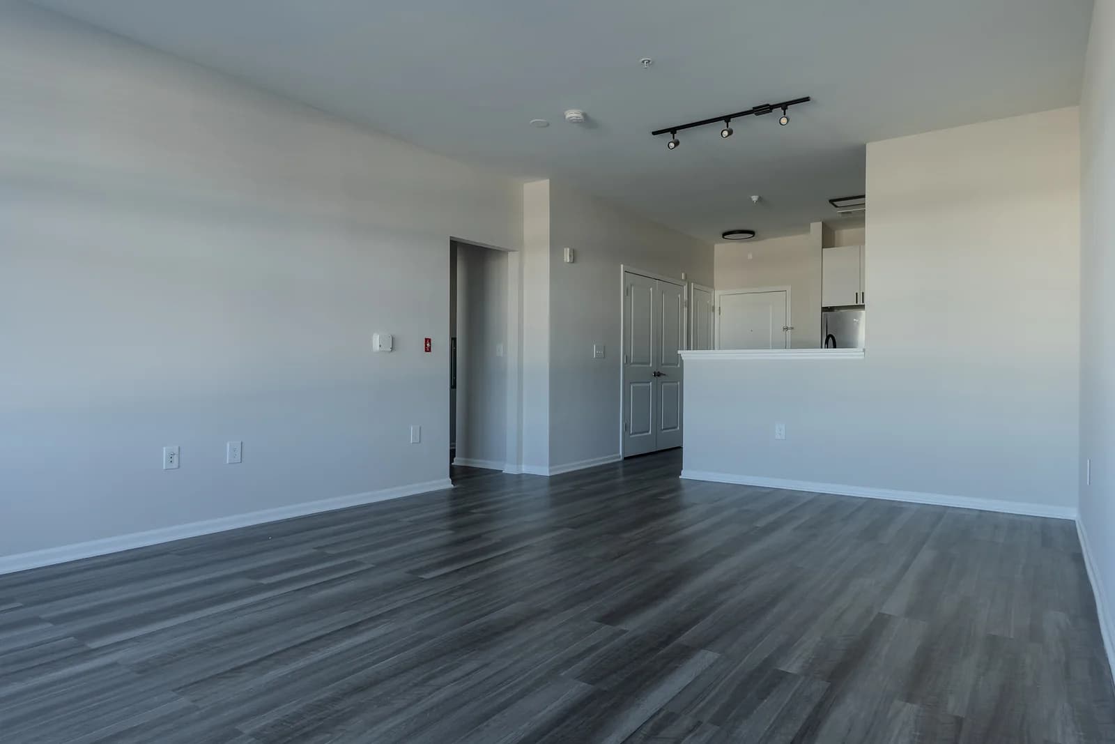 Spacious living area with gray plank floors, track lighting, and a breakfast bar opening to the kitchen.